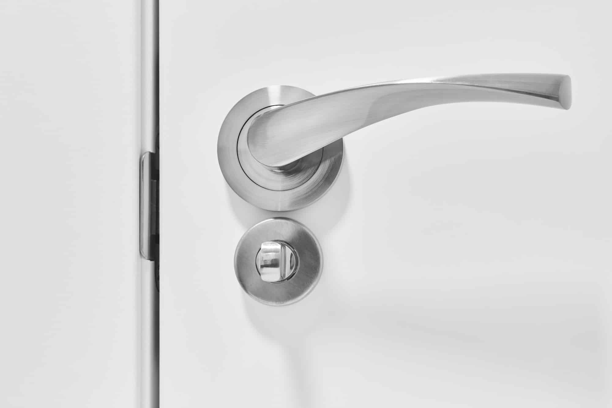 Metallic doorknob and bolt on a white wooden door. Detail